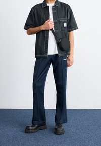 Svart- och vitt randig kortärmad skjorta, vit t-shirt, marinblå träningsbyxor, klumpiga svarta stövlar och en rund axelväska.