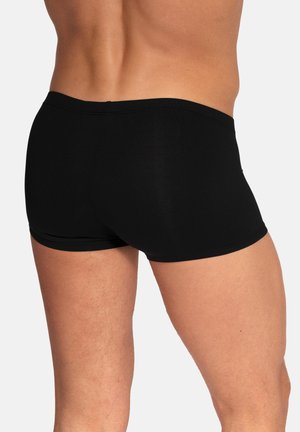 Achteraanzicht van een persoon die nauwsluitende zwarte boxer briefs draagt, waarbij taille, heupen en bovenbenen zichtbaar zijn tegen een effen achtergrond.