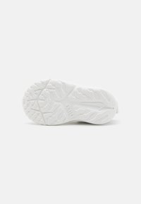 Semelle de basket blanche en caoutchouc texturé, arborant un motif en nid d'abeille et des rainures pour une meilleure adhérence, avec un logo imprimé sur le côté.