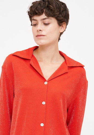 Red button-up shirt with a collar, featuring a textured fabric that sparkles. Buttons are white, and the style is loose-fitting.