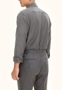 Grijze, gestructureerde blouse met opgerolde mouwen, aangevuld met grijze op maat gemaakte broeken met achterzakken en een slanke tailleband.