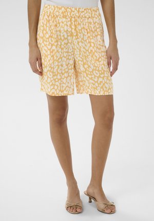Vrouw draagt gele en witte short met dierenprint, elastische tailleband en beige open-toe kitten heels.