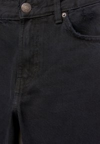 Gros plan sur la poche avant d'un jean en denim noir avec bouton en métal et rivet, montrant la texture du tissu et les détails de couture.