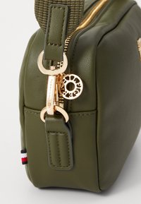 Olive green leather bag with gold hardware, featuring a zipper and visible logo charm, complemented by a matching fabric strap.