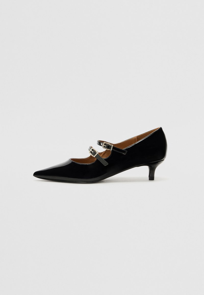 Chaussure Mary Jane en cuir verni noir avec bout pointu, deux brides à boucles argentées et un petit talon kitten, présentée sur fond uni.