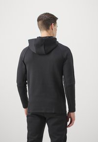 Sudadera deportiva negra con una textura suave, un diseño ajustado y capucha. Tiene mangas largas y acentos de costura minimalista.