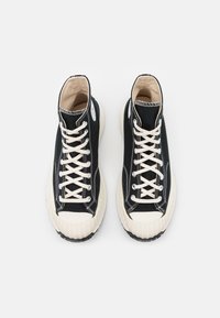 Baskets montantes noires avec des lacets blancs, semelles en caoutchouc et des détails de couture marqués. Matériau en toile avec un design à bout rond.