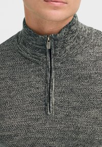 Felpa grigia con zip e colletto alto, caratterizzata da un motivo di tessuto testurizzato e una zip frontale con una finitura metallica a contrasto.