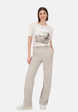 Hellbeige, locker sitzende Hosen kombiniert mit einem hellen T-Shirt mit einem Straßenmotiv, ergänzt durch weiße Sneaker.