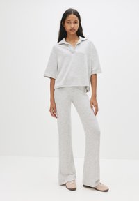 Top polo scurt din bumbac gri, cu mâneci scurte, asortat cu pantaloni evazați de aceeași culoare. Modelul poartă pantofi roz deschis.