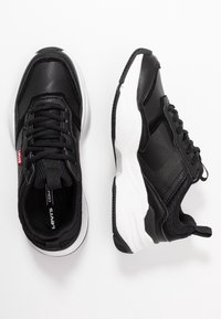 Černé tenisky s kombinací texturované kůže a síťoviny. Mají bílou podrážku, polstrovaný límec a výraznou štítek s logem.