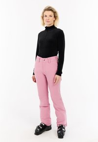 Zwarte ribgebreide longsleeve top, roze broek met riemlussen en zakken, zwarte skibotten met metalen hardware. Eenvoudig en functioneel ontwerp.
