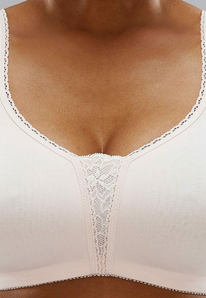 Soutien-gorge rose clair avec une texture lisse, doté d'un panneau en dentelle au centre et de surpiqûres décoratives le long des bretelles.