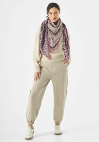 Pull en tricot beige, joggers assortis, et une écharpe à motifs avec des accents roses, comprenant un mélange de motifs animaliers dans des couleurs atténuées.