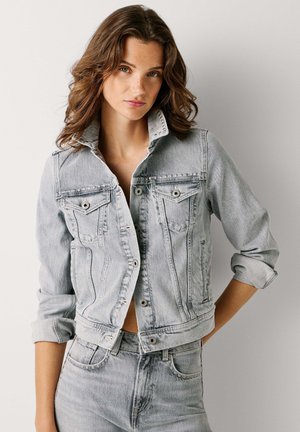 Svetlo umývaná džínová bunda s tlačnou prednou časťou, dvoma vreckami na hrudi a zvinutými rukávmi. Má klasický golier a bledú textúru.