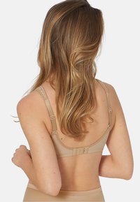 Beżowy stanik bezprzewodowy z regulowanymi ramiączkami, zapięciem na haczyk i oczko, miękką teksturą materiału i minimalistycznym wzornictwem. Posiada gładkie pokrycie pleców.
