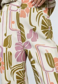 Pantalons de couleur crème clair à motif floral présentant des formes abstraites en rose, vert et orange. Tissu doux avec une coupe décontractée et fermeture à bouton.