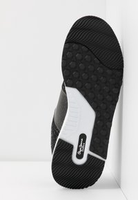 Semelle de chaussure noire et blanche avec des motifs hexagonaux et ondulés, arborant la marque "Pepe Jeans London" au centre.
