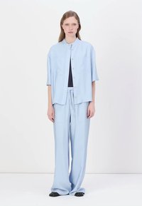 Conjunto azul claro a juego que incluye una camisa de botones de manga corta y pantalones holgados con bolsillos. Textura de tela suave y lisa.