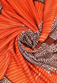 Tessuto arancione a strisce con accenti marroni, caratterizzato da un motivo a spirale e una texture liscia, piegato in forma di spirale.