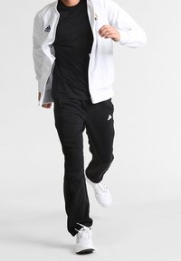 Witte zip-up jas met logo, zwart t-shirt, zwarte broek en witte sneakers; atletische pasvorm, glad materiaal, gestroomlijnd ontwerp.