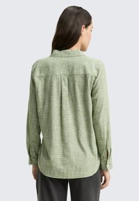 Camicia a quadri verdi con maniche lunghe, colletto a bottone e dettaglio di piega sul retro. Realizzata in un tessuto leggero e testurizzato.