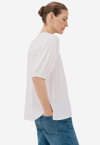 Blusa bianca leggera con maniche corte a sbuffo e vestibilità rilassata. Abbinata a jeans in denim blu, per un look casual.