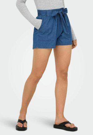 Spodnie z niebieskimi szortami z wysokim stanem typu paperbag, z przednimi kieszeniami i przewiązanym paskiem, w połączeniu z czarnymi sandałami na platformie i szarą bluzką z długim rękawem.