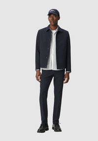 Chaqueta de marina con botones a presión, camisa blanca, pantalones oscuros y zapatos negros. La gorra presenta texto blanco, añadiendo un detalle informal al conjunto.