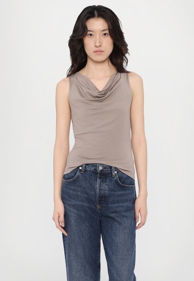 Uten ermer beige topp med drapert halslinning, kombinert med løse, mørkeblå denimjeans. Jevn tekstur av stoffet og avslappet passform.