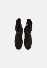 Bottines en daim noir avec fermeture éclair latérale et détail de sangle, vues de dessus sur fond blanc.
