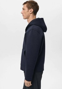 Sudadera con capucha azul marino hecha de tela suave, con un bolsillo frontal y puños acanalados. El diseño es sencillo con un ajuste relajado.