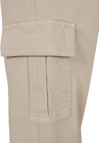 Pantalon cargo en tissu beige avec poche à rabat rectangulaire sécurisée par des coutures et des plis sous le rabat.