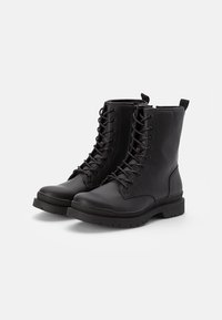 Botines de cordones negros con un upper sintético suave, puntera redonda, costuras reforzadas y suela de goma texturizada para mejorar el agarre.