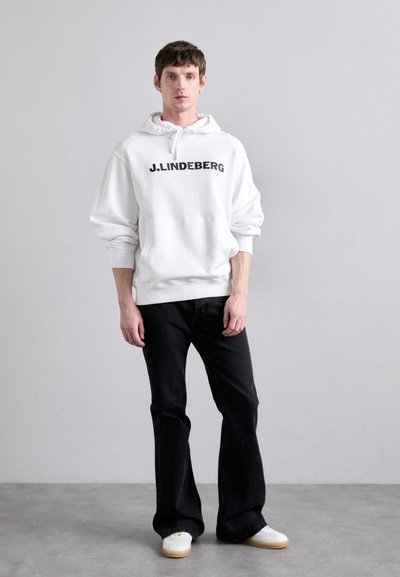 Felpa bianca con stampa nera "J.LINDEBERG", abbinata a jeans neri a palazzo e sneakers bianche. Tessuto morbido, vestibilità casual.