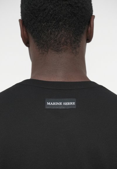 T-shirt preta de algodão com decote redondo e etiqueta com "MARINE SERRE" bordada a branco na parte superior das costas. Design simples.