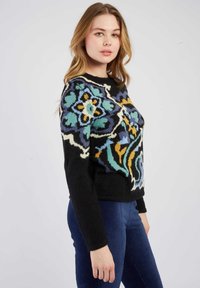 Pull en maille noir avec un design floral coloré bleu, jaune et blanc. Tissu texturé et col rond.