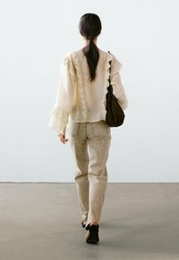 Light cream blouse with ruffled edges, paired with light beige pants. The outfit is complemented by a brown bag and black slip-on shoes.