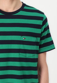 T-shirt à manches courtes en coton rayé vert et bleu marine, doté d'une poche avec un petit logo multicolore. Encolure ronde et détails de couture.
