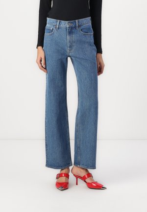 Hoge taille, wijde blauwe denim jeans met een lichte wassing, voorzien van vijf zakken en contrasterende stiksels. Gecombineerd met rode, spitse hakken.