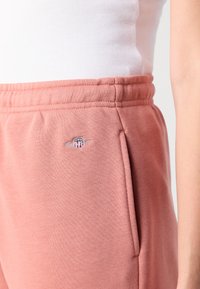 Roze sweatpants van een gestructureerde stof, met een tailleband met trekkoord en zijzakken. Geborduurd logo aan de linkerkant.