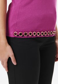 Top fucsia con orlo a scallop e dettagli in occhio d'oro. Il tessuto è morbido ed elastico, abbinato a pantaloni neri a vestibilità slanciata.