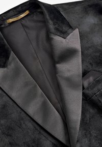 Chaqueta de terciopelo negro con cuello de satén y forro de malla en el interior, que presenta un diseño elegante y sutiles detalles de textura.