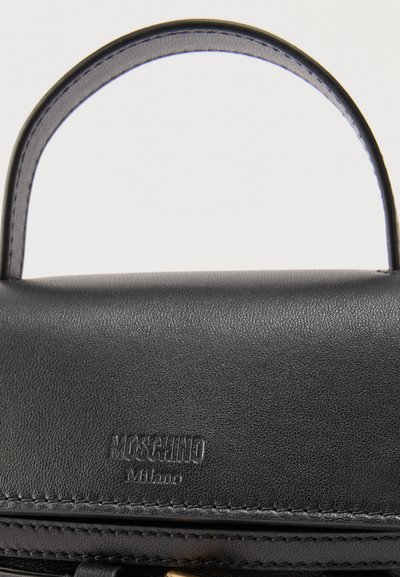 Λαβή και επάνω καπάκι από μαύρο δέρμα τσάντας χειρός με ανάγλυφο λογότυπο "MOSCHINO Milano" και εμφανείς ραφές.