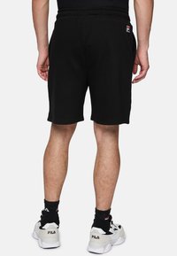 Pantaloni corti neri in cotone con vita elastica, dotati di tasche e di un'etichetta con il logo Fila sul retro. Indossati con sneakers bianche e calze nere.
