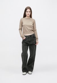 Hnědý krátký svetr s žebrovanými manžetami v kombinaci s černými širokými džíny. Modelka má na sobě bílé tenisky. Jednoduchý design bez výrazných vzorů.