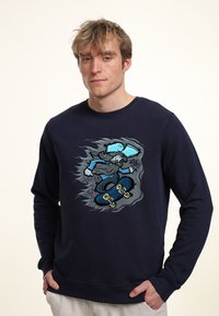 Felpa blu navy con un design grafico di uno skateboarder con un cappellino blu. Realizzata in morbido tessuto con polsini e orlo a costine.