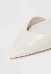 Chaussure blanche à bout pointu en cuir lisse avec un design à coupe basse. L'intérieur présente une doublure beige et des détails de couture subtils.