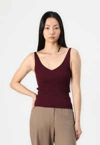 Top sin mangas de canalé burdeos con escote en forma de V y tirantes estrechos, combinado con pantalones de pierna ancha beige. Textura suave, diseño ajustado.