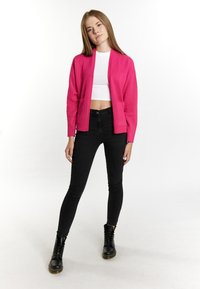Fuchsia open-front cardigan with two front pockets, worn over a white crop top, paired with black skinny jeans and lace-up black boots.